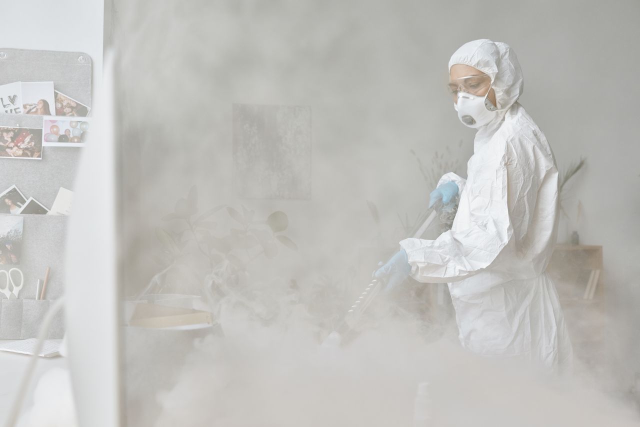 Une femme en combinaison de protection désinfecte un espace intérieur à l’aide d’un équipement de nébulisation.